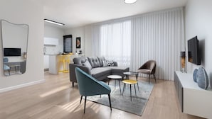 Un salon moderne avec un canapé d’angle gris, un fauteuil bleu et une petite table basse. On y trouve également un coin cuisine avec un tabouret de bar jaune et une table à manger. Un téléviseur à écran plat est fixé au mur, et un luminaire au plafond est visible.