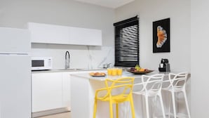 Une cuisine moderne avec des meubles blancs, un four à micro-ondes, un évier et un bar pour prendre le petit-déjeuner, agrémenté de tabourets de bar jaunes et blancs.