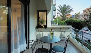 A balcony with a round table, two bar stools, and a potted plant. - Loftstyle Beach in Gordon By Holyguest (Tel Aviv-Yafo)