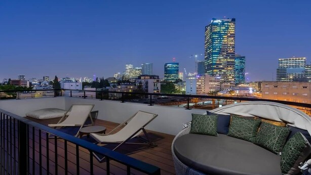 Eine Dachterrasse mit Liegestühlen und einer Sitzecke, mit Blick auf eine städtische Skyline in der Abenddämmerung.