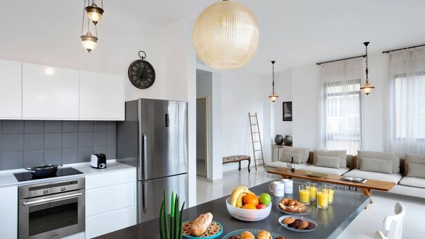 A modern kitchen with stainless steel appliances, a central island with breakfast items, and a dining area with a sofa and coffee table.