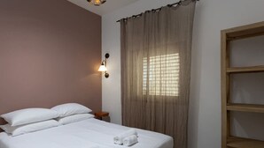 A hotel room with a bed, a nightstand, a wall-mounted lamp, and a window with curtains.