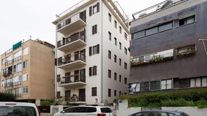 A multi-story residential building with balconies, a parking area, and a neighboring building.