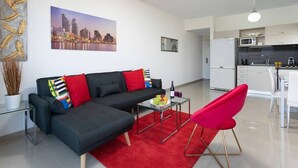A modern living room with a black sofa, red and multicolored cushions, a glass coffee table with fruit and wine, and a red chair. - Pinsker 1BR corner Bograshov by HolyGuest (Tel Aviv-Yafo)
