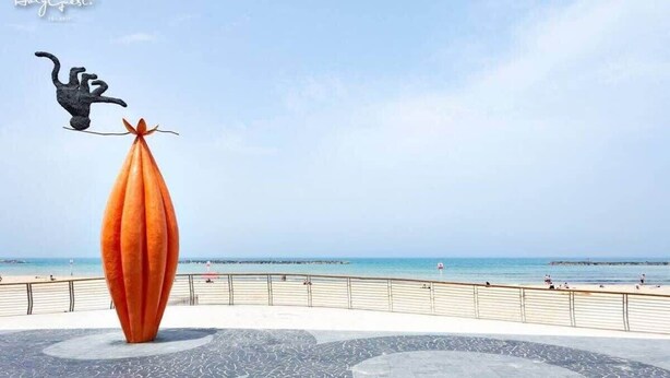 A beach with a large orange sculpture and a black figure balancing on top. - Pinsker 1BR corner Bograshov by HolyGuest (Tel Aviv-Yafo)