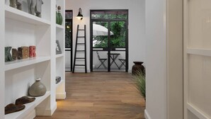 A hallway with wooden flooring, white shelves with various decorative items, a ladder, and a view of a patio with chairs and an umbrella. - Hip 2BR in Reines by HolyGuest (Tel Aviv-Yafo)