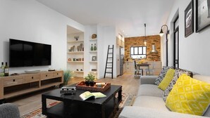 A modern living room with a flat-screen TV, a coffee table with books, a sofa with patterned cushions, and a kitchen area with a brick wall and wooden cabinets. - Hip 2BR in Reines by HolyGuest (Tel Aviv-Yafo)