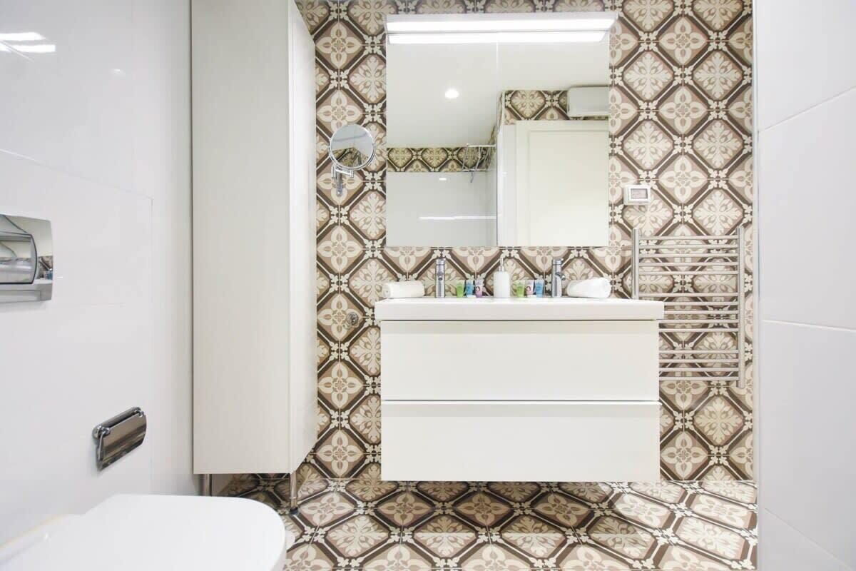 A bathroom with patterned wallpaper, a white vanity, and a mirror above the sink.