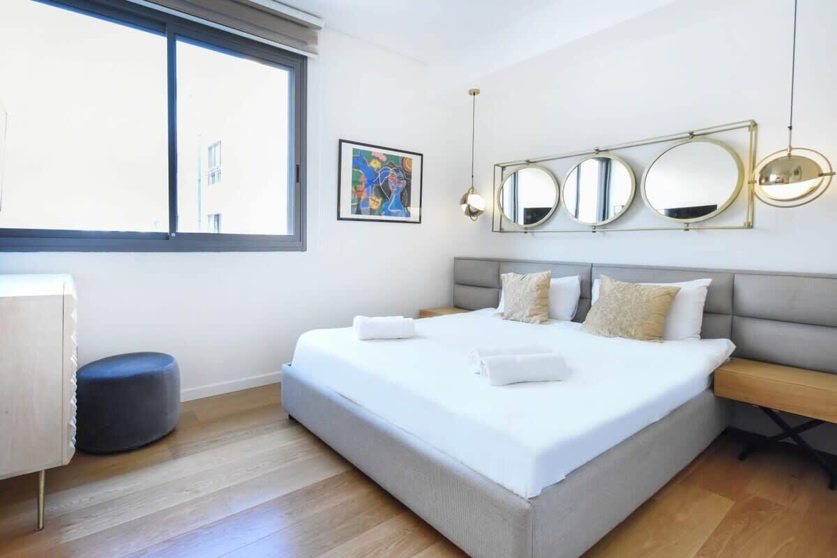 Une chambre moderne avec un grand lit, une table de chevet, un banc et une fenêtre.