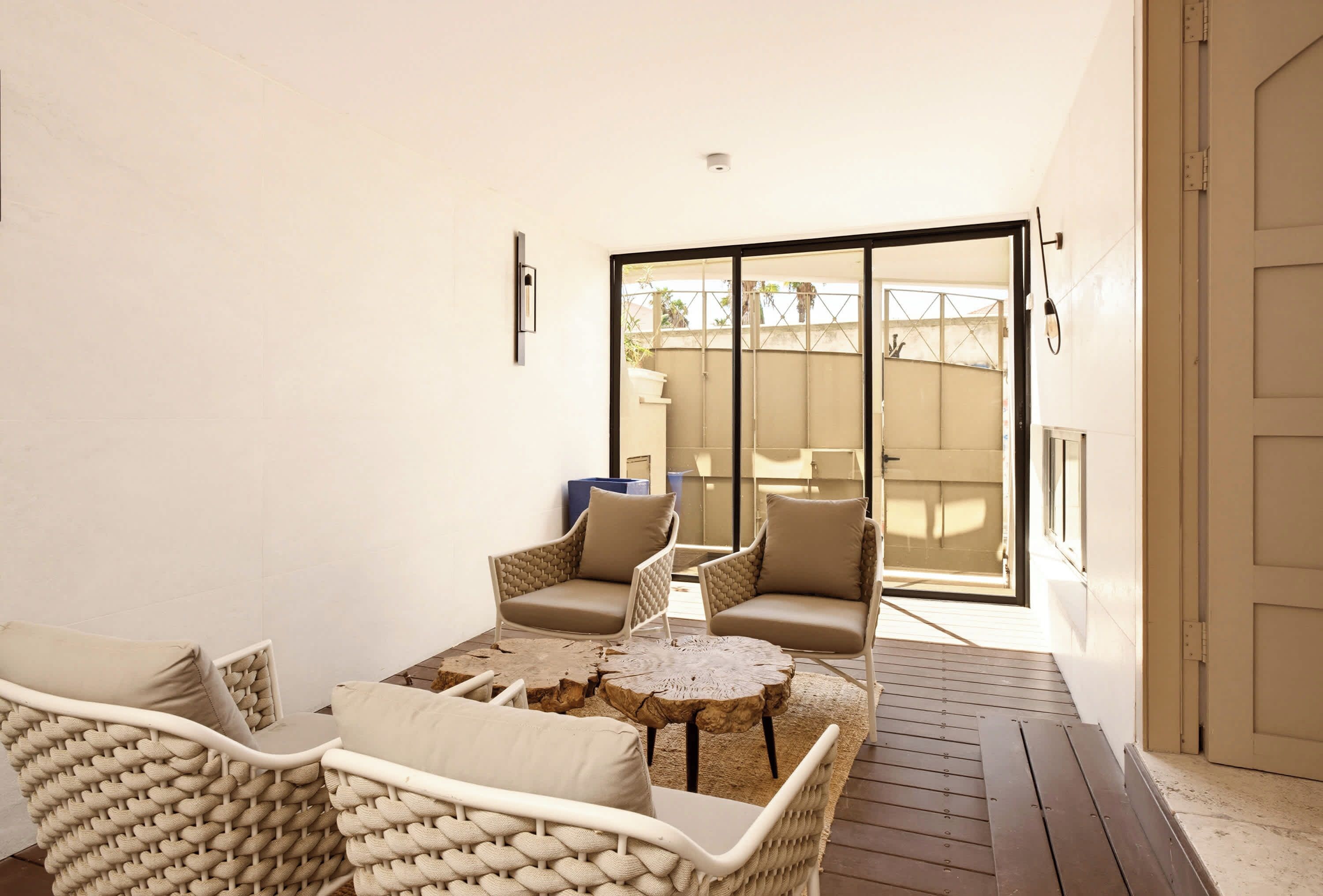 Une terrasse ensoleillée, meublée de meubles en osier, avec une petite table ronde et une porte-fenêtre coulissante donnant sur un espace extérieur abrité.