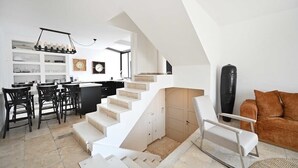 Un intérieur moderne avec un escalier menant à une mezzanine, une cuisine dotée de tabourets de bar et un coin salon avec un canapé et un fauteuil.