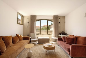 Un salon comprenant un canapé, un fauteuil, un pouf, une table basse et une petite table d’appoint avec une lampe.