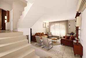 Un salon moderne avec un escalier, un ensemble de canapés, une table basse et une lampe.