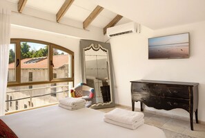 A bedroom with a large window, a bed, a dresser, and a mirror.