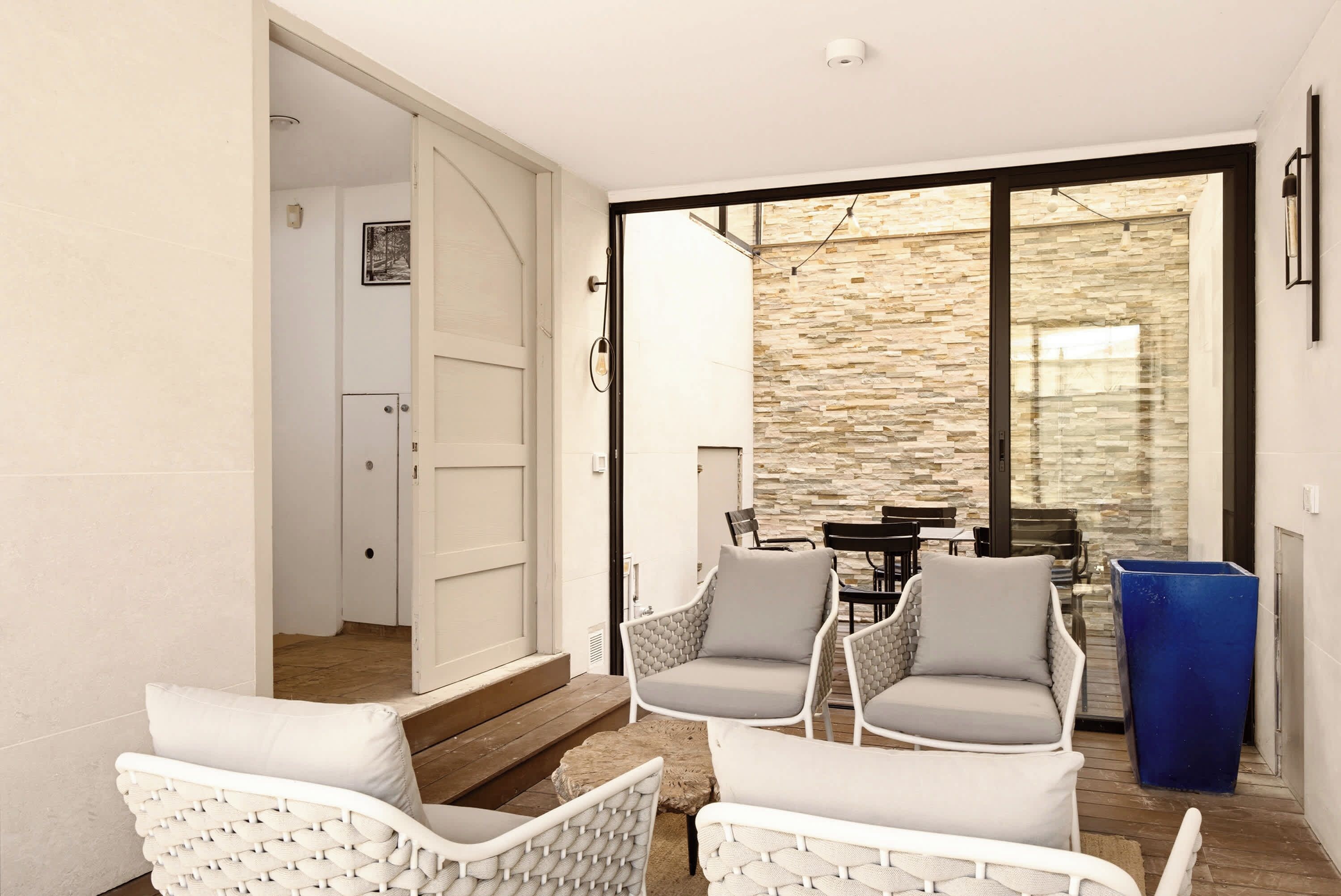 Un espace patio aménagé avec des chaises et une table en osier, un mur en pierre et une porte donnant sur un espace intérieur.