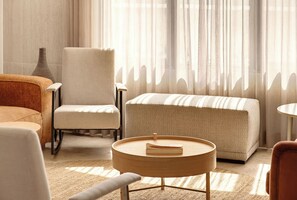 A cozy living room with a sofa, armchair, and ottoman, a vase, and a window with sheer curtains. - 4BR Family House in Neve Tsedek with Mamad by Holyguest (Tel Aviv-Yafo)