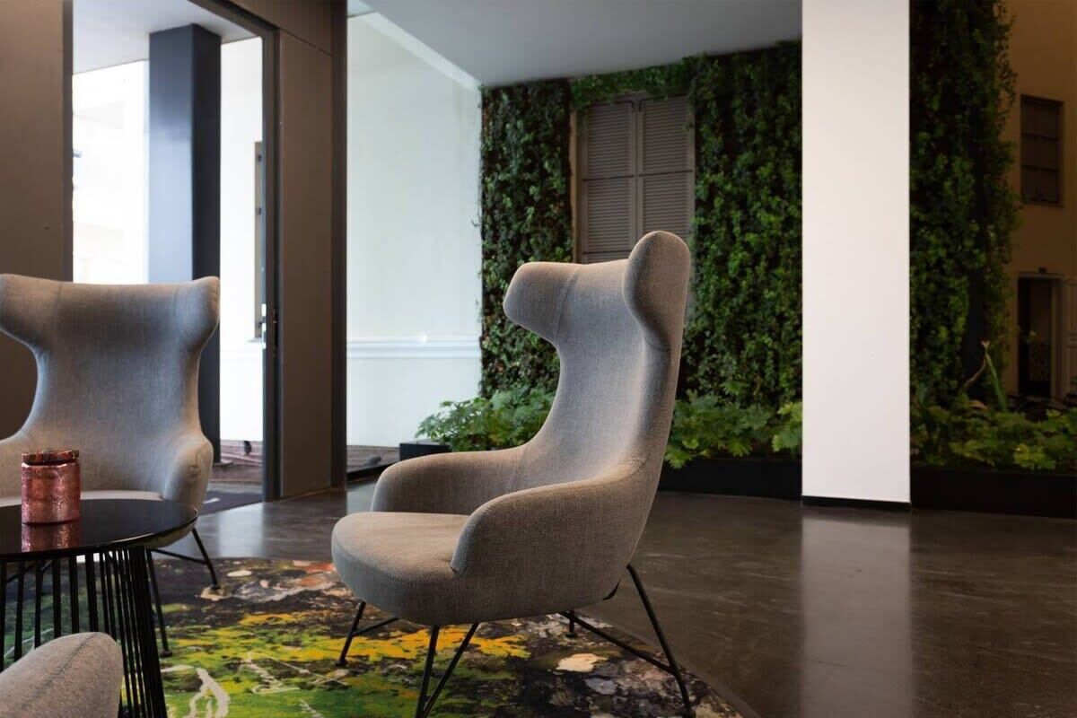 A modern interior with a unique chair design, a textured rug, and a green wall with climbing plants.