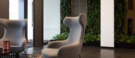 A modern interior with a unique chair design, a textured rug, and a green wall with climbing plants.