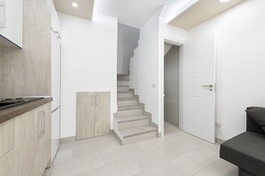 A modern kitchen with a built-in stove, a staircase leading to a second floor, and a door to a bedroom.
