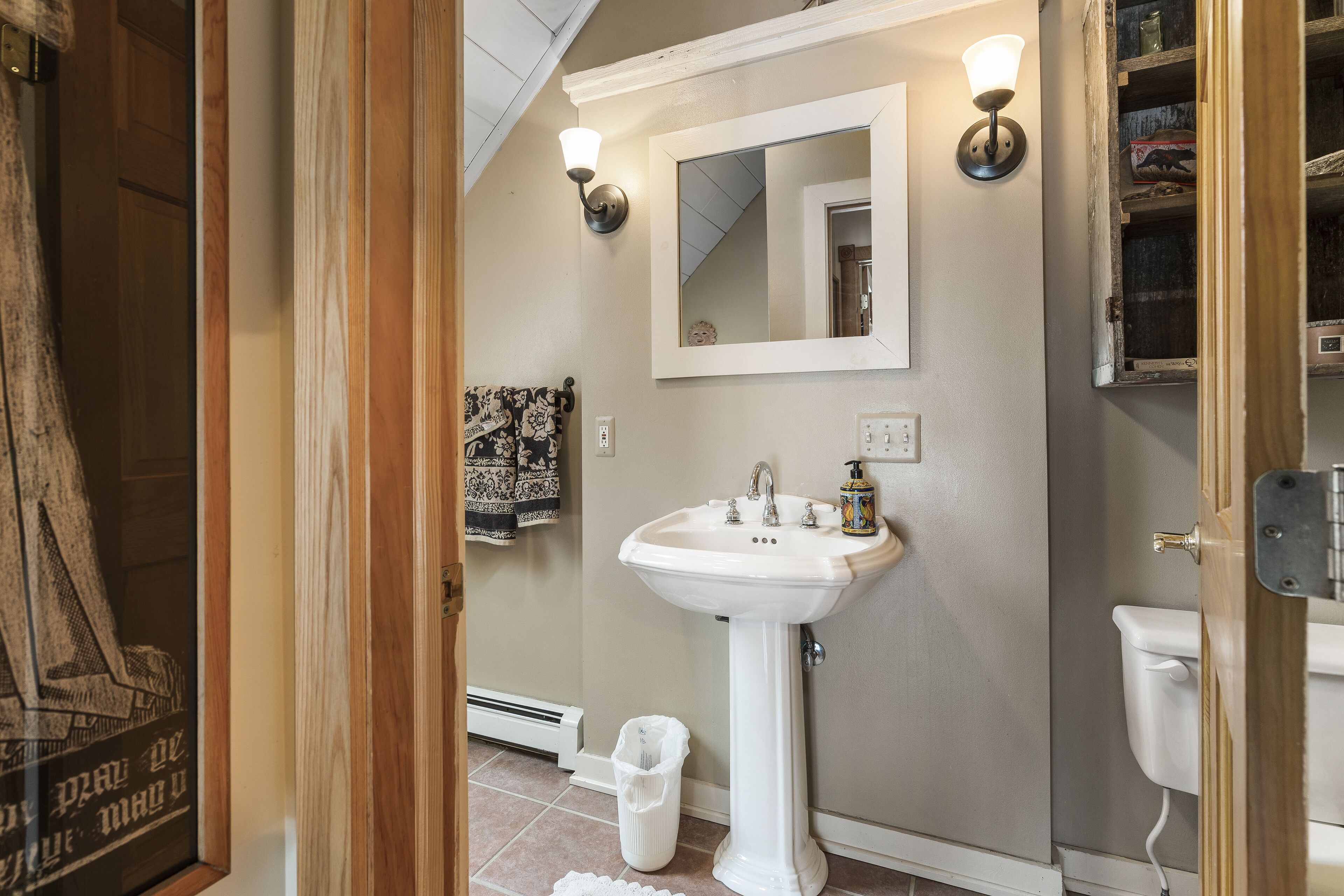 A bathroom with a pedestal sink, a mirror, and a toilet.