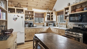 A kitchen with wooden cabinets, a stove, a microwave, and various kitchen appliances. - Quiet Cabin in the Woods - Secluded Yet Close to It All (Levering)