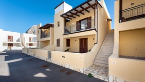 Um edifício residencial com escadaria que dá para uma varanda, degraus de pedra e céu claro.