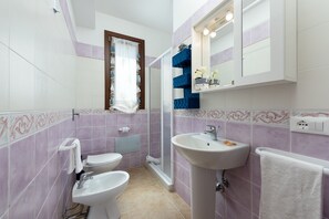 Een badkamer met toilet, bidet, wastafel en douche.