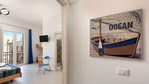 A room with a bed, a chair, a TV, and a painting of a boat on the wall.