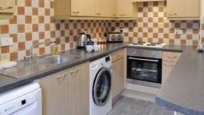 A kitchen with wooden cabinets, a washing machine, a dishwasher, a stove, and a tiled backsplash.