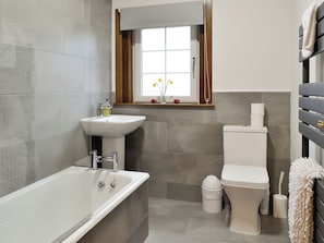 Et moderne badeværelse med badekar, vask, toilet og et vindue med blomster.