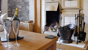 Um quarto aconchegante com lareira, parede de pedra e mesa de madeira com copos e garrafa.
