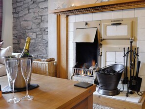 A cozy room with a fireplace, a stone wall, and a wooden table with glasses and a bottle. - Baldowrie Farm Cottage (Kettins, near Blairgowrie)