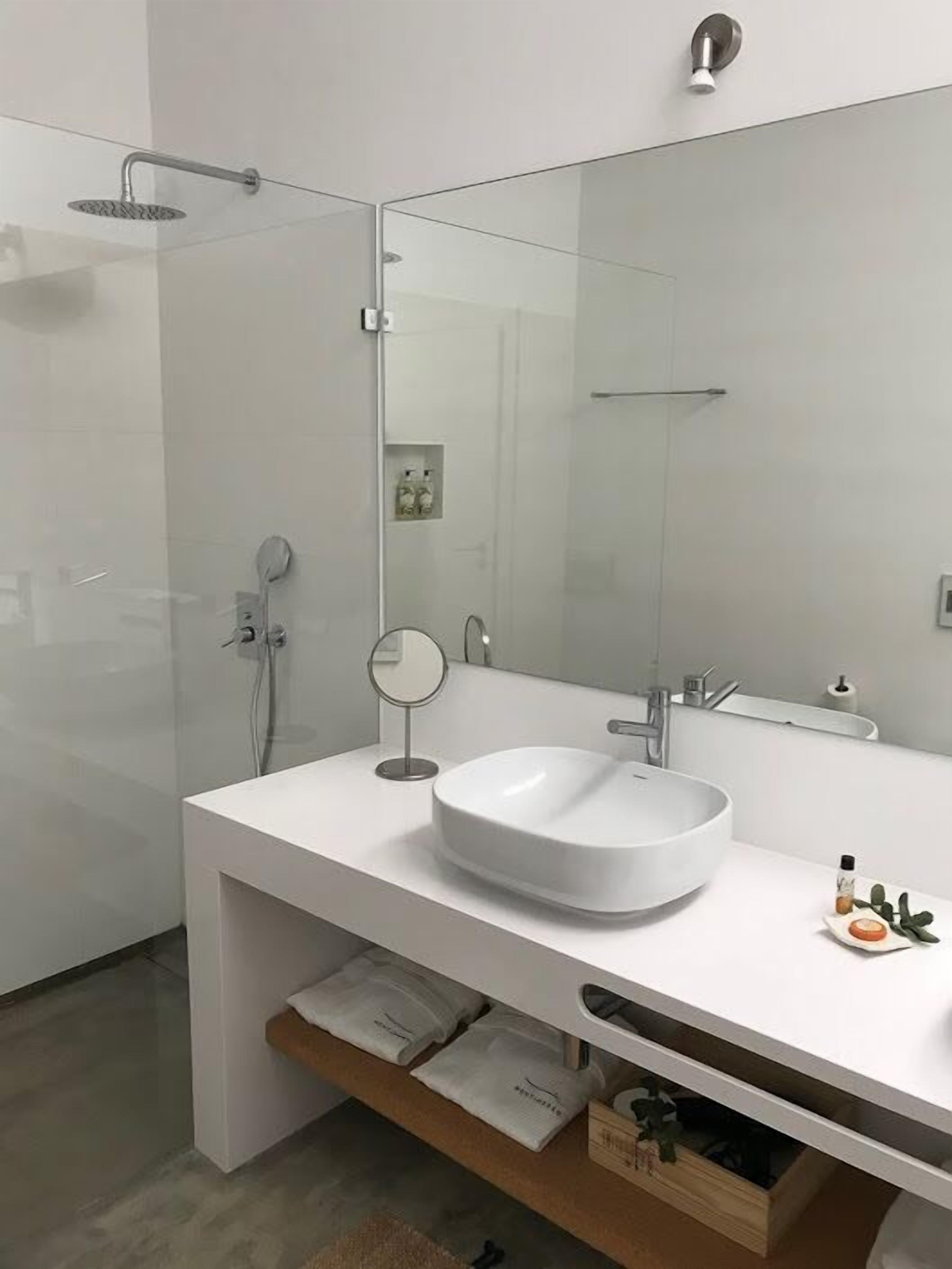 Un baño moderno con un espejo grande, un lavamanos redondo y una ducha.