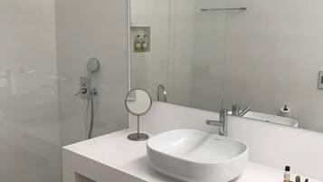 Un baño moderno con un espejo grande, un lavamanos redondo y una ducha.