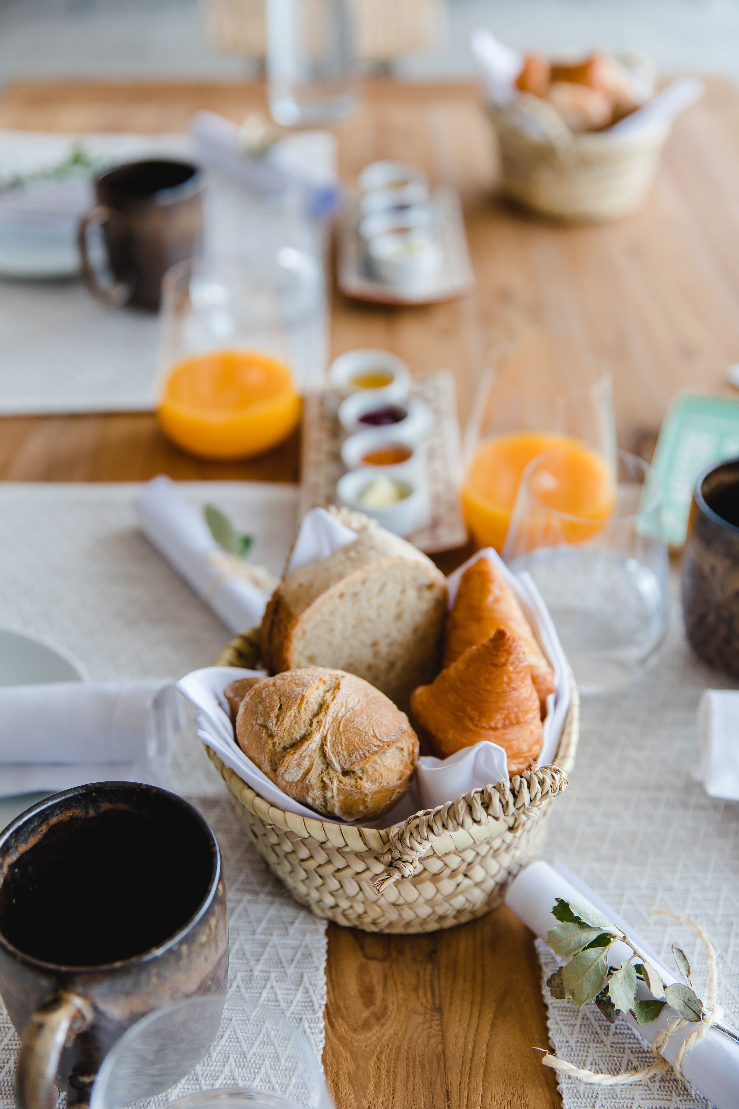 A breakfast setting with bread, pastries, and orange juice on a wooden table.