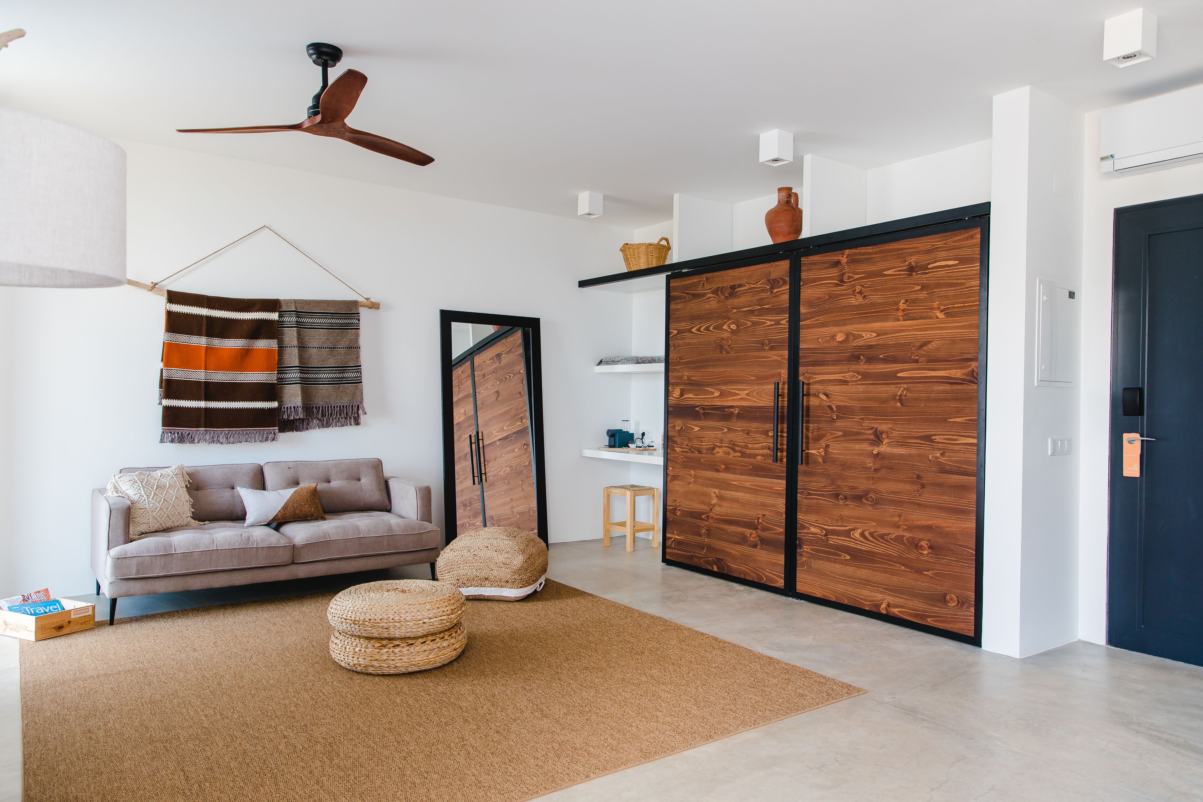 A modern living room with a sofa, ottomans, a hanging blanket, a wooden wardrobe, and a ceiling fan.