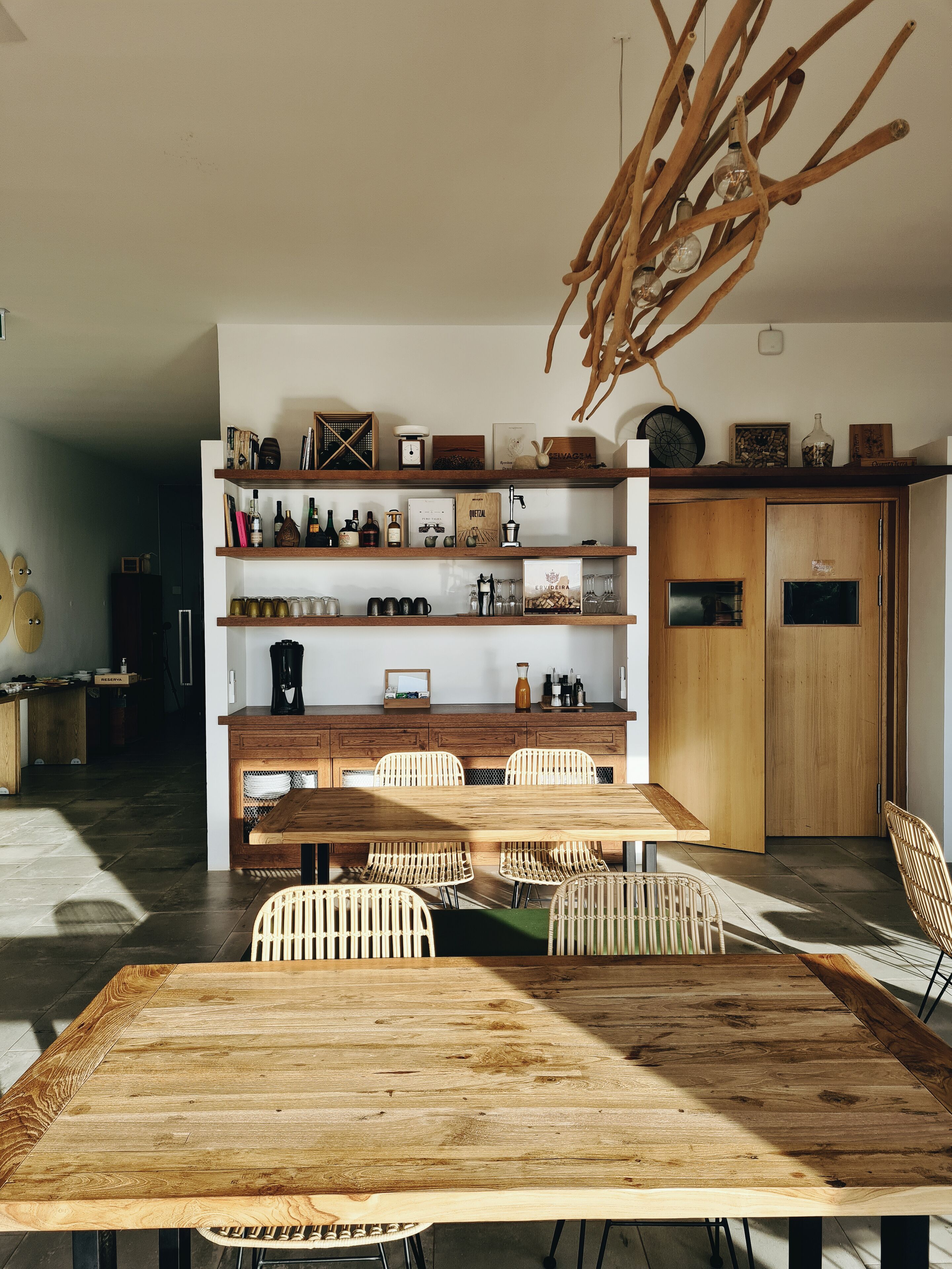 Una cocina moderna con una mesa de comedor de madera, sillas de mimbre y una estantería empotrada con diversos objetos.