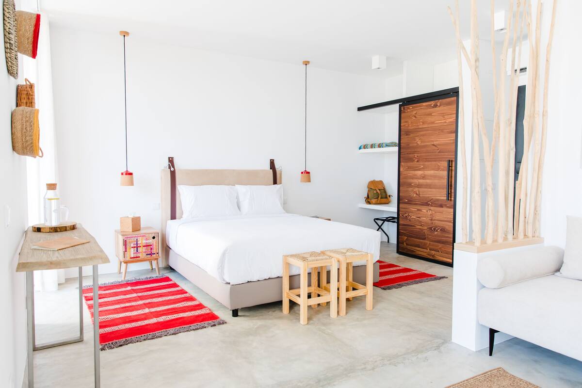 Ein modernes Schlafzimmer mit einem Bett, Holzschemeln, einem kleinen Tisch und einem roten Teppich.