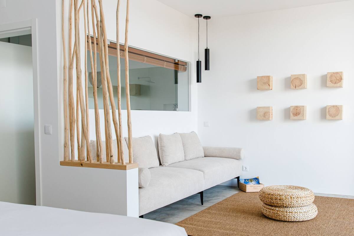 Ein modernes Schlafzimmer mit einem großen Bett, einer Couch, einem hängenden Holzbild und einem roten Teppich mit Muster.