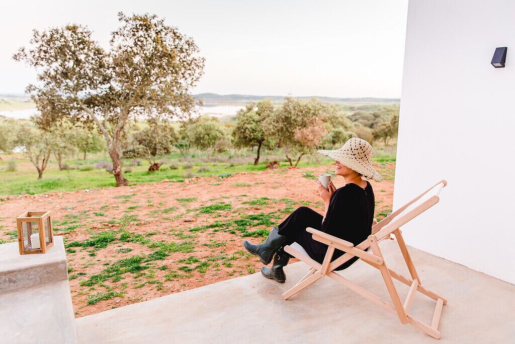 A person sitting on a wooden chair in a room with a view of a landscape with trees and a body of water.