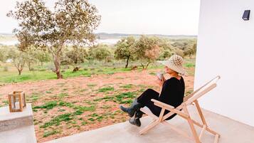 A person sitting on a wooden chair in a room with a view of a landscape with trees and a body of water.