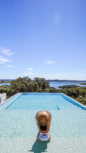 A pool with clear water, surrounded by greenery and a view of a lake and hills. - Montimerso Skyscape Country House  (Reguengos de Monsaraz)