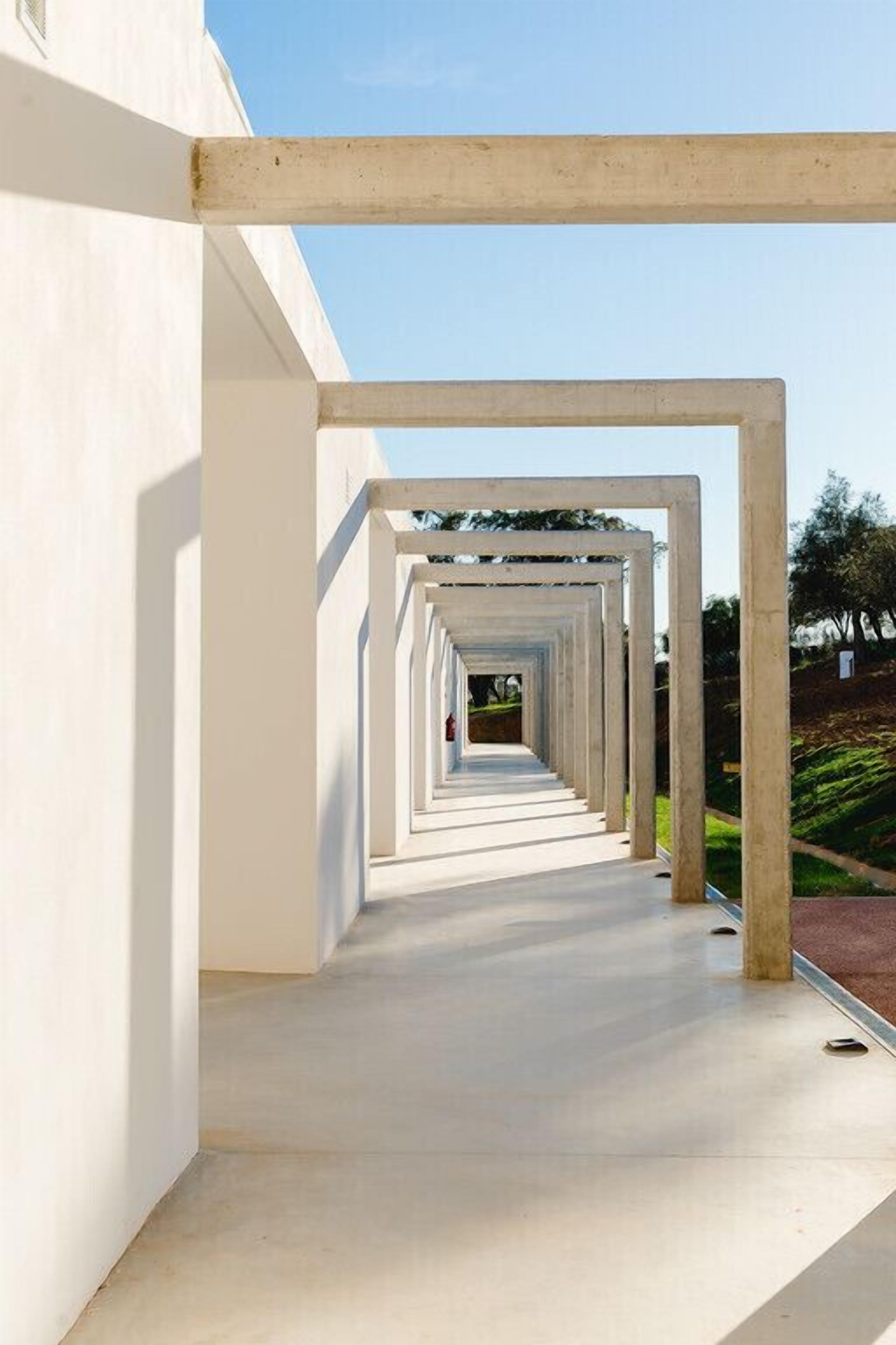 Un couloir bordé d’une série de cadres blancs qui mène à l’entrée d’un bâtiment.