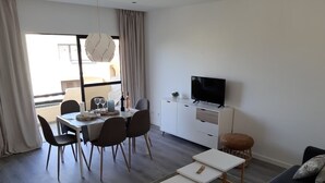 Een moderne woonkamer met een eethoek, een flatscreen televisie en een bank.