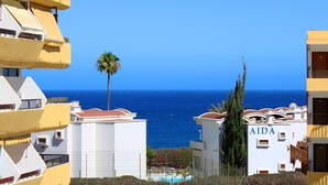 A coastal hotel with a pool, palm trees, and clear blue skies.