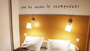 A hotel room with a wooden headboard, two bedside lamps, white bedding, and a brown throw blanket.