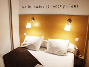 A hotel room with a wooden headboard, two bedside lamps, white bedding, and a brown throw blanket.
