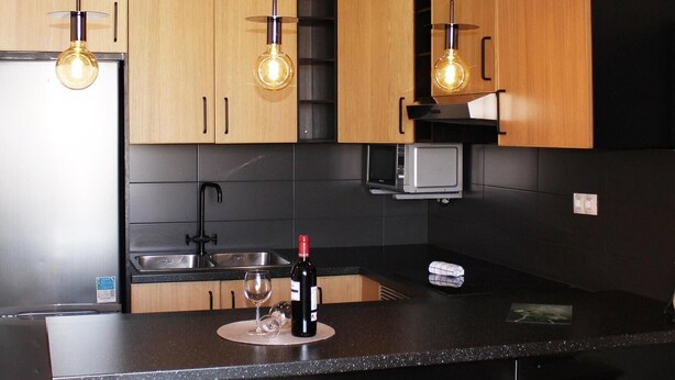 A modern kitchen with wooden cabinets, a black countertop, and pendant lighting.