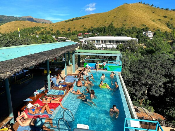A pool area with lounge chairs and umbrellas, surrounded by greenery and hills. - Outpost Hostel - Coron - Adults Only (Coron)