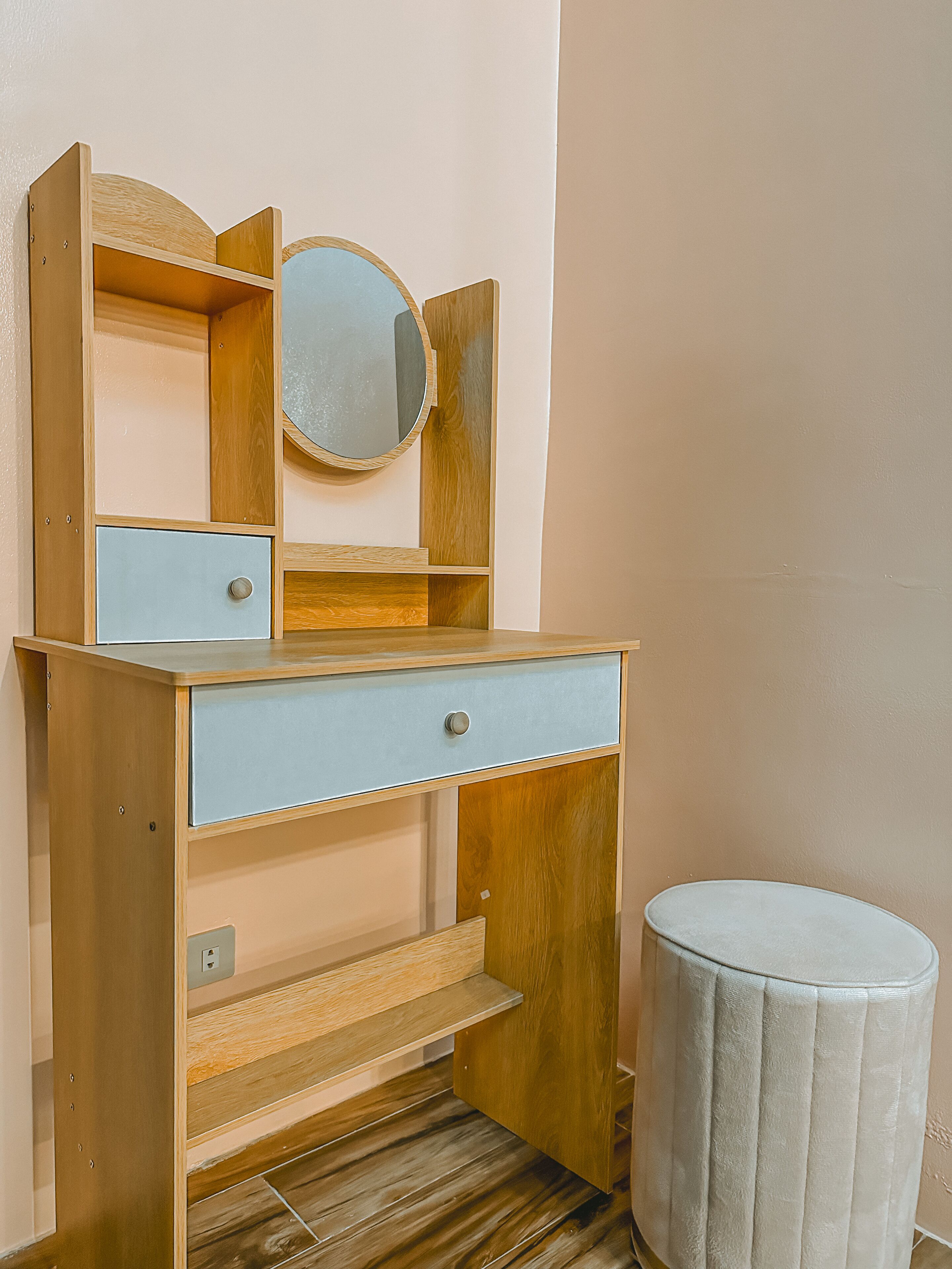Een houten wastafelmeubel met spiegel, twee lades en een klein krukje.